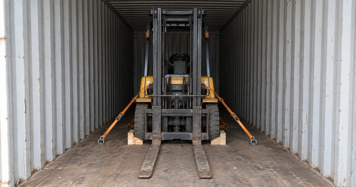 Yellow forklift chocked with timber and strapped to floor rings inside a shipping container