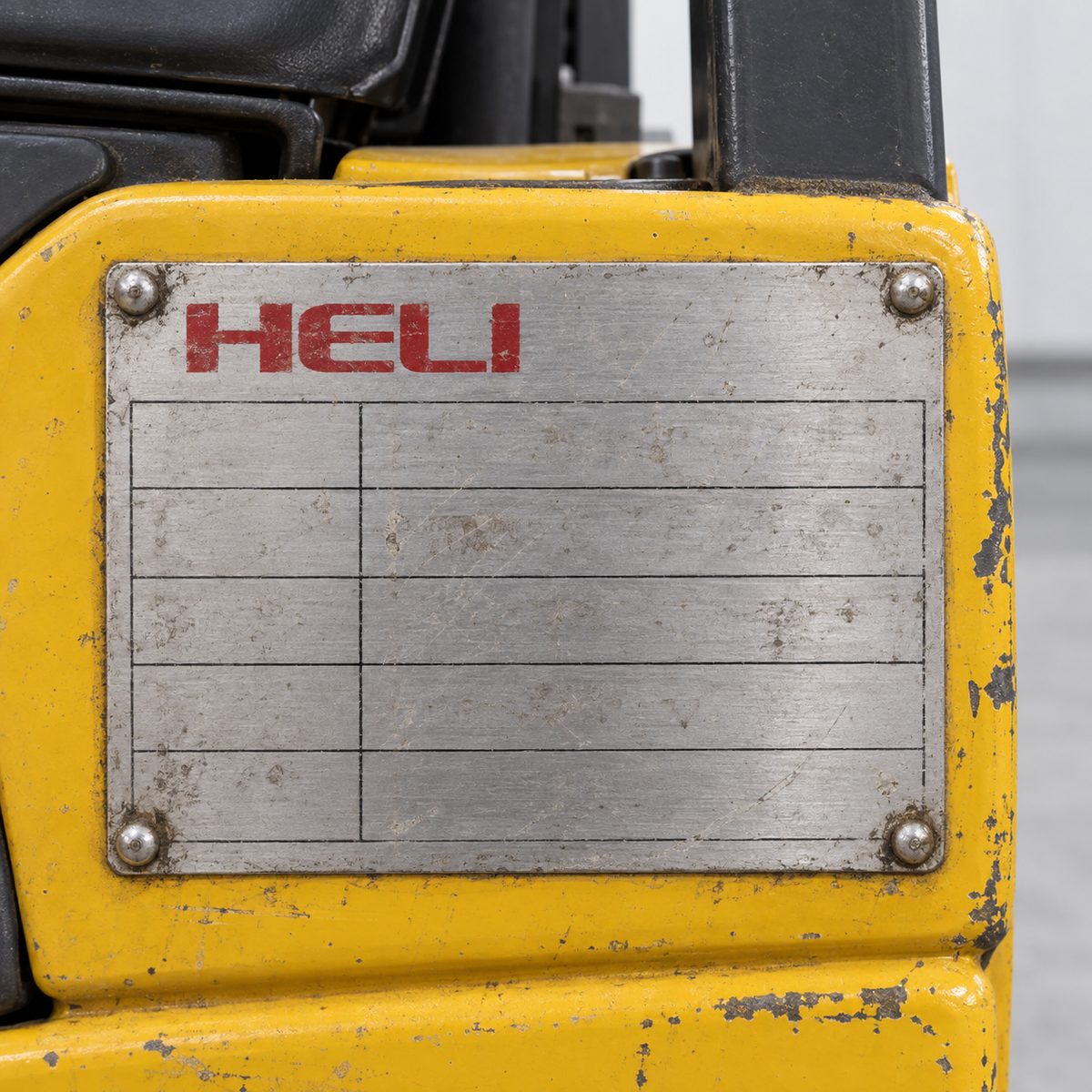 Worn aluminium data plate with red Heli name riveted to a yellow forklift cowl
