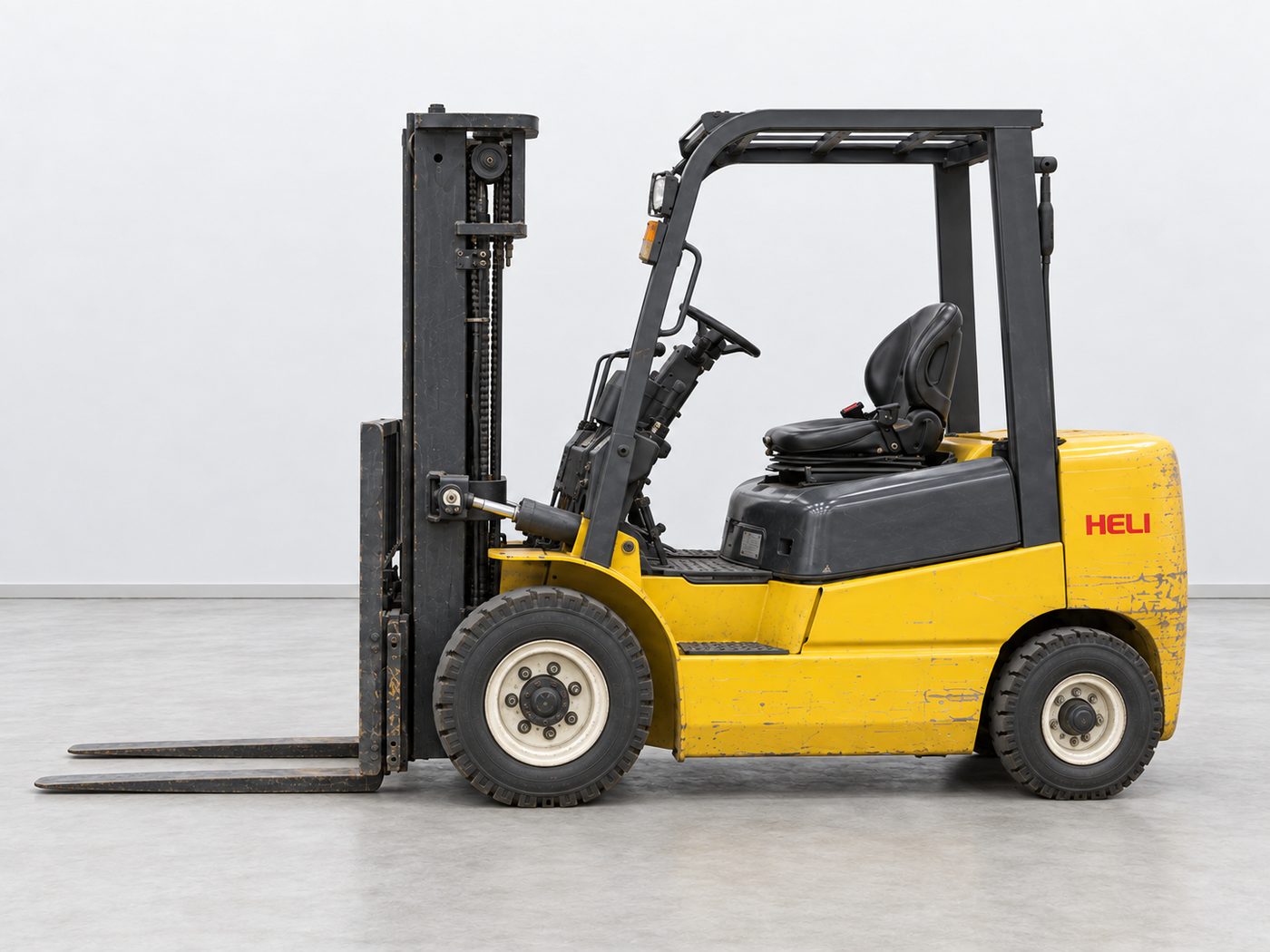 Side view of a used yellow Heli forklift with black mast, forks lowered and empty seat